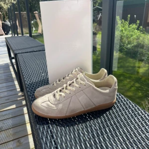 Beige sneakers från Maison Margiela - Säljer ett par stilrena beige sneakers från Maison Margiela med klassisk design och gummisula. Skorna har rund tå, platt sula och är tillverkade i mocka med diskreta sömdetaljer. Ingår dustbags. Det är storlek 42 men passar 42,5 till 43. Kvitto finns och är köpta ifrån farfetch!