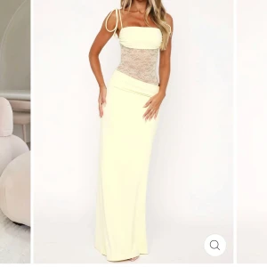 Ljusgul långklänning med spetsdetaljer -  Säljer en ljusgul långklänning med smala axelband och transparent spets i midjan. Klänningen har en figurnära passform upptill och raka linjer nertill. Perfekt för sommarens tillfällen när du vill sticka ut lite extra. Klänningen är helt ny och aldrig använd 