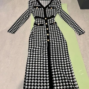 Svartvit långklänning  - Snygg långklänning i svart och vitt med klassiskt hundtandsmönster. Klänningen har lång ärm, v-ringning och dekorativa guldknappar framtill samt svarta detaljer vid fickor och midja. Perfekt för dig som vill sticka ut med en tidlös look.