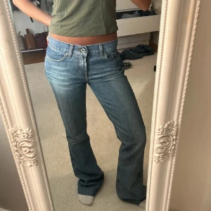 Lågmidjade bootcut jeans i blå denim - Säljer ett par klassiska blå jeans med låg midja och bootcut passform. Jeansen har fem fickor, bälteshällor och stängs med dragkedja och knapp. Perfekta för dig som gillar en tidlös och avslappnad stil.