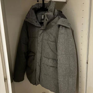 Grå pufferjacka med huva från Dressmann - Säljer en grå pufferjacka från Dressmann i storlek M. Jackan har huva, dragkedja och stora fickor framtill. Perfekt för kyliga dagar och enkel att matcha med olika outfits. Nypris 1,399kr säljer den för 550 men kan sänkas vid snabb affär. Kan lämnas i Kristianstad, Malmö eller Lund.