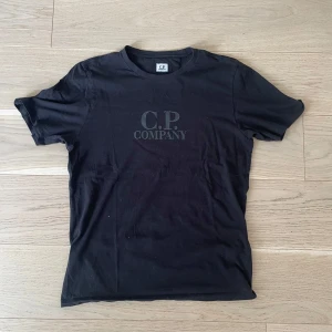 Svart t-shirt från C.P. Company - Svart t-shirt från C.P. Company med diskret logga tryckt på bröstet. Klassisk rund hals och korta ärmar. Perfekt för en clean och stilren look.
