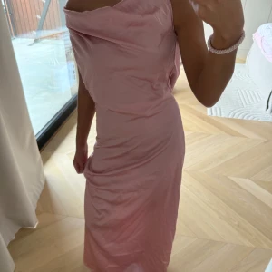 Ljusrosa långklänning med öppen rygg - Säljer denna  ljusrosa långklänning med draperad framsida och öppen rygg med knytband. Klänningen är i satin. Perfekt för bal.