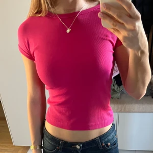 Rosa croppad ribbad t-shirt - Säljer en snygg croppad t-shirt i stark rosa färg. T-shirten är ribbad och har korta ärmar samt rund halsringning.