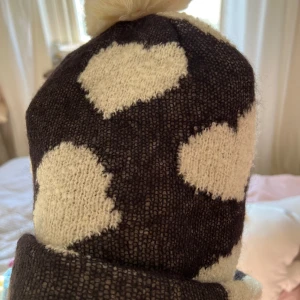 Svart och vit stickad mössa med tofs från Ivana Helsinki - Mysig svart stickad mössa med stora vita prickar och en fluffig tofs på toppen. Märke Ivana Helsinki. Perfekt för kalla dagar och har en uppvikt kant för extra värme.