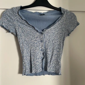 Blommig blå topp från Monki - Söt ljusblå topp från Monki med små vita blommor, ribbad struktur och korta ärmar. 🌸🌸