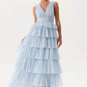 Ljusblå volangklänning med v-ringning - Säljer en drömmig ljusblå långklänning med flera lager volanger och djup v-ringning både fram och bak. Klänningen har ärmlös design och markerad midja, perfekt för bal eller fest. Materialet är lätt och ger en svävande känsla. Helt ny med prislapparna kvar🩵