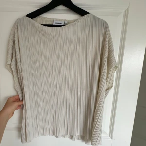 Plisserad vit topp från Weekday - Säljer en vit plisserad topp från Weekday med lös passform och korta ärmar. Toppen har rund halsringning och är tillverkad i ett lätt syntetmaterial. Perfekt för en stilren och modern look.