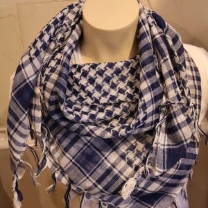 Palestina sjal Blåvit rutig halsduk med fransar - Säljer en blåvit halsduk med rutigt mönster och dekorativa fransar i kanterna. Halsduken är mjuk och luftig, perfekt att svepa runt halsen för en snygg och avslappnad stil.