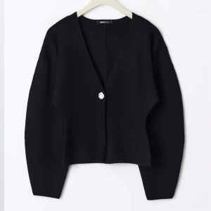 Svart figursydd kofta med v-ringning och knapp - Säljer en svart figursydd kofta med v-ringning och en dekorativ knapp framtill. Koftan har långa ärmar med lätt puff och är tillverkad i ett mjukt material. Perfekt att styla med jeans för en clean look.