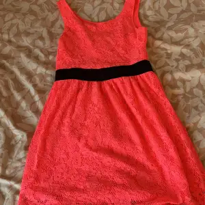 Säljer en söt korallfärgad klänning från H&M med spetsdetaljer och svart midjeband. Klänningen är ärmlös och har en rund halsringning. 💗