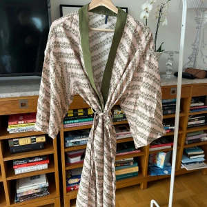 Mönstrad kimono med gröna detaljer - Säljer en elegant kimono med ett blommigt mönster i grönt på en ljus bakgrund. Den har en kontrasterande grön krage och knyts med ett bälte i midjan. Perfekt för en avslappnad stil.