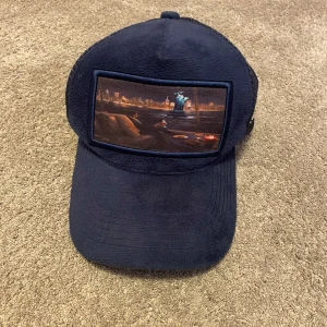 Mörkblå keps - Snygg mörkblå keps från NATONE med nätpaneler för extra ventilation. Framsidan har en unik bilddetalj som ger kepsen en cool look. Perfekt för varma dagar eller som en stilren accessoar.