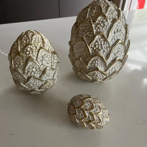 Dekorativa guldiga påskägg i 3 storlekar  - Säljer ett set med tre dekorativa kottar i olika storlekar. De är gjorda i ett material som liknar sten och har en vit och guldaktig färg. Perfekt för att ge en naturlig och elegant touch till inredningen. Passar bra som bordsdekoration eller i hyllor. Perfekt för påsken 