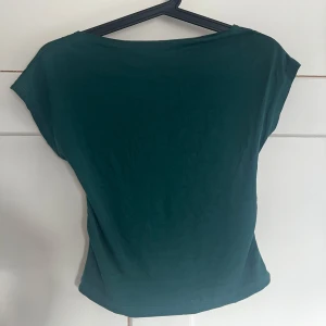 Mörkgrön topp med öppen rygg - Snygg mörkgrön topp med öppen rygg och korta ärmar. Perfekt för en stilren och avslappnad look. Passar bra till både jeans och kjol.