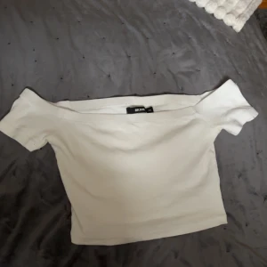 Vit offshoulder topp från Bik Bok - Säljer en stilren vit offshoulder topp från Bik Bok. Toppen har en tight passform och är perfekt för en trendig look. Den är tillverkad i ett mjukt material som känns skönt mot huden. Perfekt för att styla med både jeans och kjol.