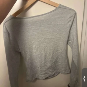 Grå långärmad topp med öppen rygg - Snygg grå långärmad topp med en stilren öppen rygg. Perfekt för en trendig look. Tillverkad i ett mjukt och bekvämt material.