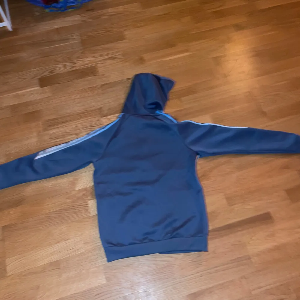 Säljer ett blått träningsset från McKenzie med byxor och huvtröja. Byxorna har elastisk midja och vita detaljer på benen. Huvtröjan har dragkedja och vita paneler på framsidan samt en huva. Perfekt för sport och fritid.. Muu.