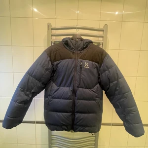 Blå och svart dunjacka från Haglöfs - Säljer en blå och svart dunjacka från Haglöfs. Jackan har en dragkedja framtill och är långärmad med en huva. Perfekt för kalla dagar. Haglöfs-loggan syns på bröstet. Nypris 4 500 Kr
