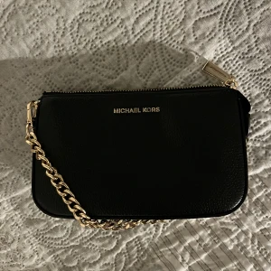 Svart handväska från Michael Kors - Snygg svart handväska från Michael Kors med guldfärgad kedja och dragkedja. Som ny!! Använd bara 2 gånger. Säljer pga att jag köpt en ny Michael kors väska.