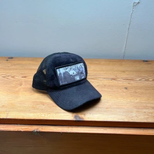 Valvet keps - Snygg svart keps med justerbar rem och nätpanel för ventilation. Oberservera att ena ”ploppen” har lossnar litegrann men den funkar fortfarande att använda 