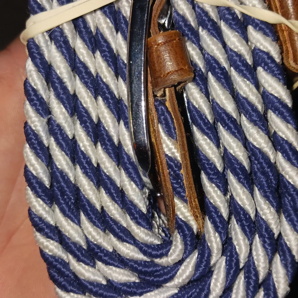 Säljer ett snyggt randigt bälte i blått och vitt med bruna läderdetaljer. Bältet har en stilren design med ett silverfärgat spänne. Perfekt för att ge din outfit en extra touch.. Muu.