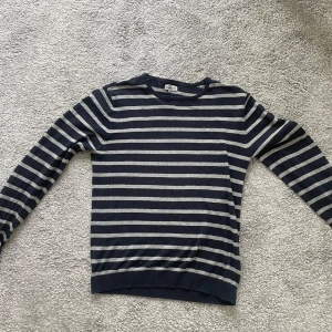 Randig tröja - Säljer en stilren randig tröja i blått och grått. Tröjan har långa ärmar och en rund halsringning, perfekt för en avslappnad look. Passar mig bra som är 180cm 66kg