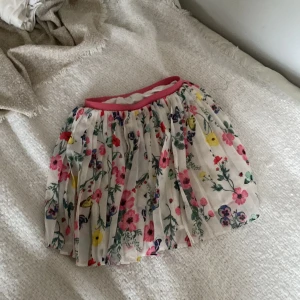 Super söt blommig kortkjol med rosa detaljer.  - Charmig kortkjol med ett färgglatt blommönster och en rosa resår i midjan. Perfekt för en somrig look! Den är i mycket bra skick och fåtal använd. Inga hål. Inga fläckar 