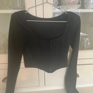 Svart topp - Säljer en stilren  topp med långärmade ärmar och  hackar  framtill för att knäppa. Kort modell! 