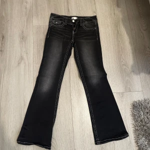 Svarta bootcut jeans från Gina Tricot - Snygga svarta bootcut jeans från Gina Tricot med kontrastsömmar och två knappar i midjan. Perfekta för en stilren look med en touch av retro. De har fickor både fram och bak.