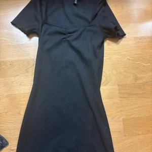 Svart ribbad klänning - Snygg svart ribbad klänning med korta ärmar och en subtil rynkdetalj vid bysten. Perfekt för en stilren look. Passar bra till både vardag och festliga tillfällen.