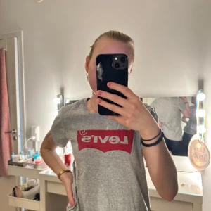 Grå t-shirt från Levi's - Säljer en klassisk grå t-shirt från Levi's med det ikoniska röda logotyptrycket på bröstet. T-shirten har en normal passform och korta ärmar, perfekt för en avslappnad stil.💞