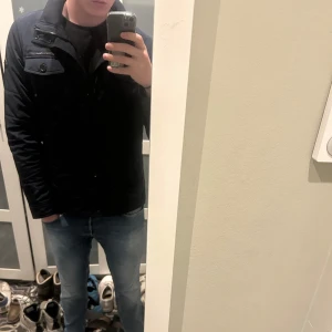 Mörkblå jacka från J.Lindeberg - Säljer en stilren mörkblå field jacket från J.Lindeberg. Jackan har långa ärmar och stängs med både dragkedja och knappar. Den har praktiska fickor med lock och en diskret logga på ärmen. Bara höra av sig vid funderingar!