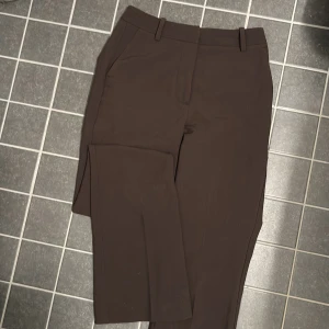 Bruna kostymbyxor från Bik Bok - Snygga bruna kostymbyxor från Bik Bok i storlek 34. Byxorna har en klassisk design med dragkedja och knappar framtill. Perfekta för en stilren look.