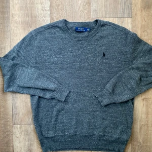 Grå tröja stickad  Polo Ralph Lauren - Säljer en stilren grå tröja från Polo Ralph Lauren med broderad logga på bröstet. Tröjan har långa ärmar och är tillverkad i ett mjukt material som passar perfekt för kyligare dagar. Perfekt för dig som gillar klassisk design!