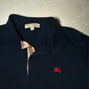 Burberry pikétröja  - Färgen är marinblå och storlek är M. Superfin och elegant tröja för killar, tjockare material än vanliga blusar. Färgar inte av i tvätten. Nackdelen är att mörka fläckar kan framträda på bilder tagna i starkt ljus, men dessa är inte synliga vid normal användning. Skriv för fler bilder