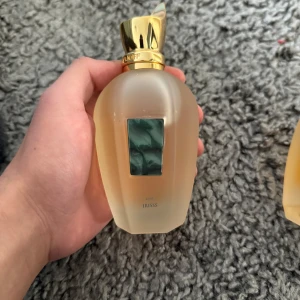 Parfymflaska med guldlock - Elegant parfymflaska med ett lyxigt guldlock och en frostad glasdesign. Flaskan har en grön dekorativ detalj på framsidan som ger en exklusiv känsla. Perfekt för den som vill ha en stilren och sofistikerad doftupplevelse.