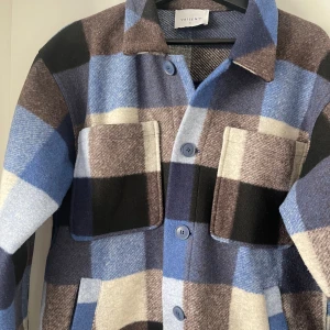 Rutig overshirt/jacka från Vailent - Säljer en oanvänd snygg rutig overshirt från Vailent i blå, brun, svart och beige. Jackan har långa ärmar och knappar framtill. Perfekt för lager-på-lager-stil eller bara som en stilren jacka till din vardagliga outfit. Nypris: 1299kr