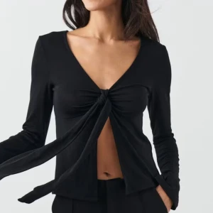 Svart v-ringad topp med knyt från Gina tricot - Snygg svart topp med v-ringning och knyt framtill. Långärmad design som passar perfekt för en stilren look. Perfekt för både vardag och festliga tillfällen.