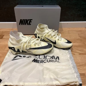 Nike Mercurial Superfly 9 Elite FG - Säljer ett par Nike Zoom Mercurial Superfly 9 Elite FG fotbollsskor i en stilren vit och svart design. Skorna har en strömlinjeformad form med snörning och är perfekta för att lira fotboll i. Fick dessa i present och då köptes dom i 1 storlek större än vad jag vanligtvis har. Tanken var att min fot skulle växa men det verkar dem inte göra. HELT NYA. Levereras med originalförpackning och påse.