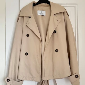 Beige trenchcoat från Stradivarius - Snygg beige trenchcoat från Stradivarius med knappar och knytbälte i midjan. Perfekt för våren🌷🌼🌿