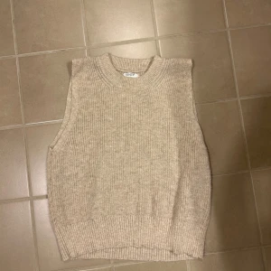 Beige stickad väst från ONLY - Säljer en stilren beige stickad väst från ONLY. Perfekt för lager-på-lager och ger en mysig känsla. Västen har en ribbad kant vid ärmhålen och nederkanten.