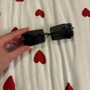 Svarta rektangulära solglasögon - Snygga svarta rektangulära solglasögon med guldfärgade detaljer. Perfekta för en stilren look. Glasögonen har en minimalistisk design med tunna skalmar.