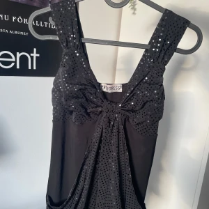 Black y2k top from Progress - Snygg svart topp från Progress med glittriga detaljer. toppen har breda axelband och en draperad design framtill. Perfekt för en kväll ute eller en speciell tillställning. Tillverkad i polyester och elastan för en bekväm passform. inte mycket utrymme för stora bröst dock tyvärr :(💘