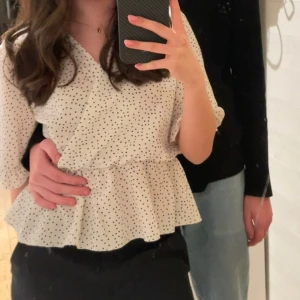 Prickig blus  - Säljer en söt vit omlottblus från Boohoo med svarta prickar. Blusen har en volangdetalj vid midjan. Perfekt till alla tillfällen. Köpt för 299 kr. Är i storlek s men passar xs då jag vanligtvis brukar bära det 