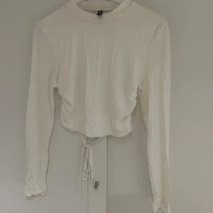 Vit långärmad topp med öppen rygg - Säljer en stilren vit långärmad topp med öppen rygg och knytning i midjan. Perfekt för en trendig look. Toppen är croppad och har en enkel design som passar till många olika outfits.