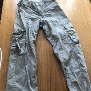 Beige cargobyxor med dragkedja - Säljer ett par beige cargobyxor från Lindex. Byxorna har flera praktiska fickor och en dragkedja framtill. De har elastisk midja och justerbara band vid bensluten för en bekväm passform.