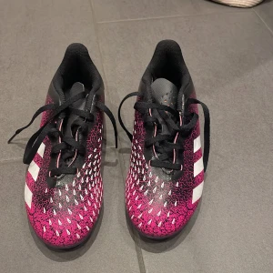 Adidas fotbollsskor i rosa och svart - Snygga Adidas fotbollsskor i en cool rosa och svart färgkombination med vita detaljer. Skorna har snörning och en mönstrad yta som ger extra grepp på planen. Perfekta för fotbollsspelare som vill sticka ut!.Skorna har använts 3 tillfällen.Säljer pågrund av att jag har växt ur dom.