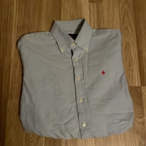 Blå skjorta från Morris - Snygg blå skjorta från Morris med klassisk krage och knappar framtill. Den har en broderad röd detalj på bröstet som ger en stilren touch. Perfekt för en elegant look. Kolla gärna in butiken, möjlighet för bundle finns.