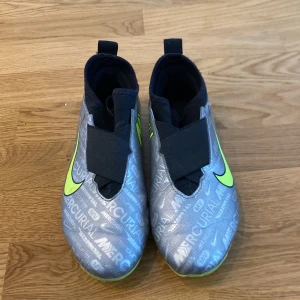 Nike Mercurial fotbollsskor - Snygga Nike Mercurial fotbollsskor i silver med neongula detaljer. Skorna har en modern design med snörningsfri överdel och tydliga logotyper. Perfekta för fotbollsplanen med sin strömlinjeformade passform.